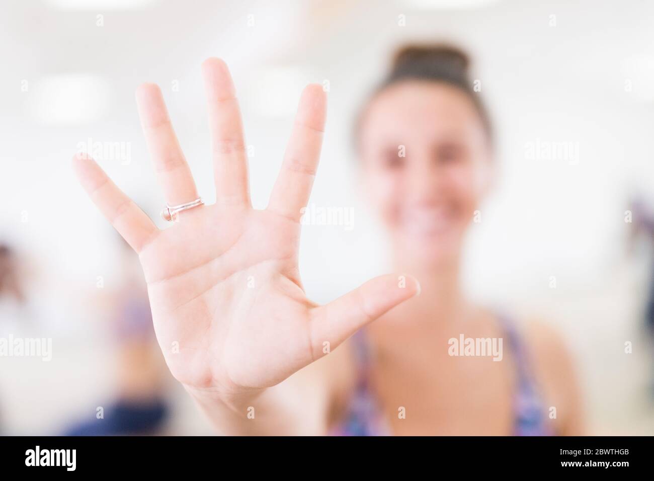Fit sportlich aktive Frau lächelnd, in Mode-Sportbekleidung zeigt eine offene Handfläche an der Kamera im Yoga-Studio. Aktiver urbaner Lifestyle. Stockfoto