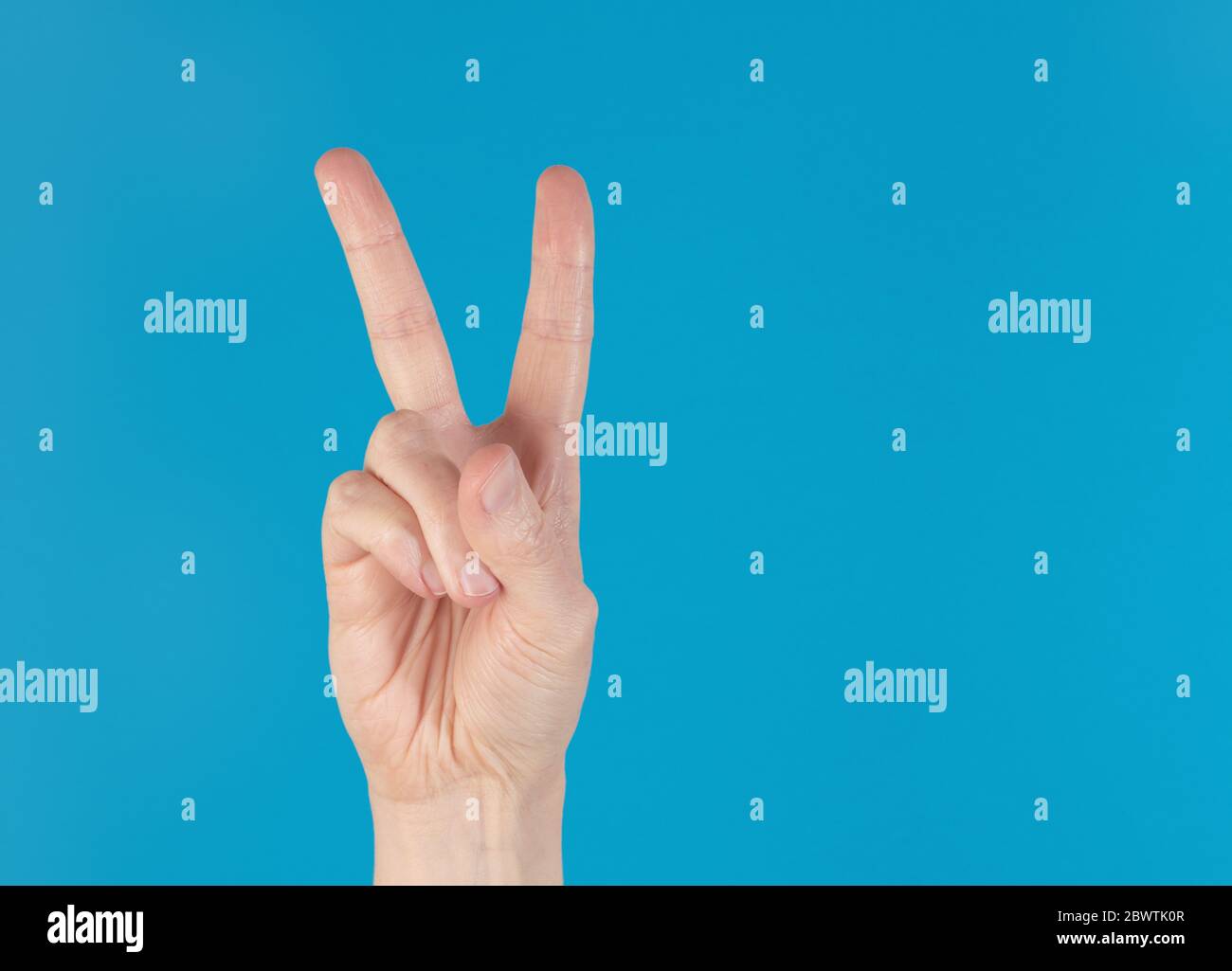 Hand macht eine Geste des Friedenszeichens, isoliert vor blauem Hintergrund Stockfoto