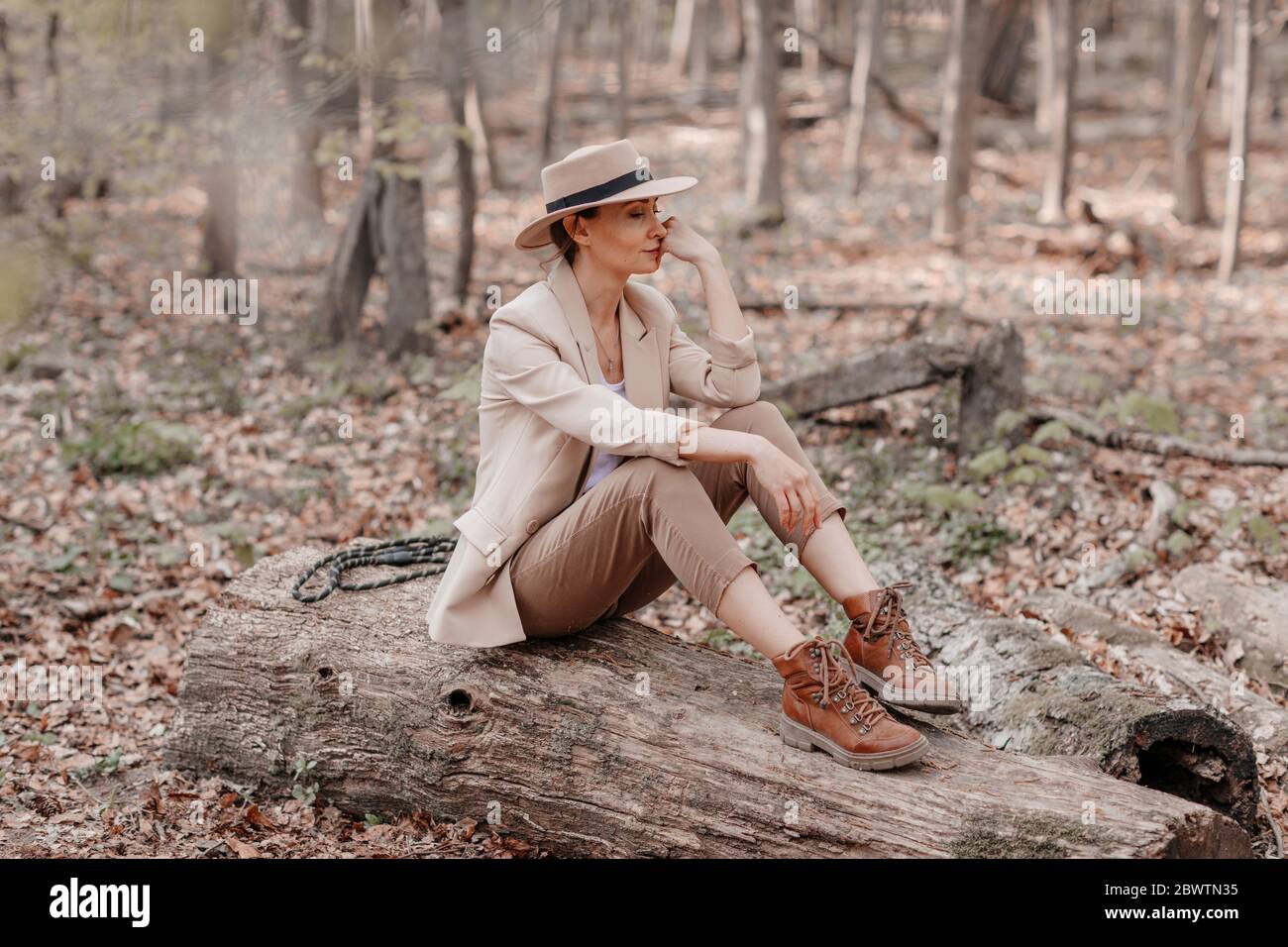 Modische Frau sitzt auf einem Holzstück im Wald Stockfoto