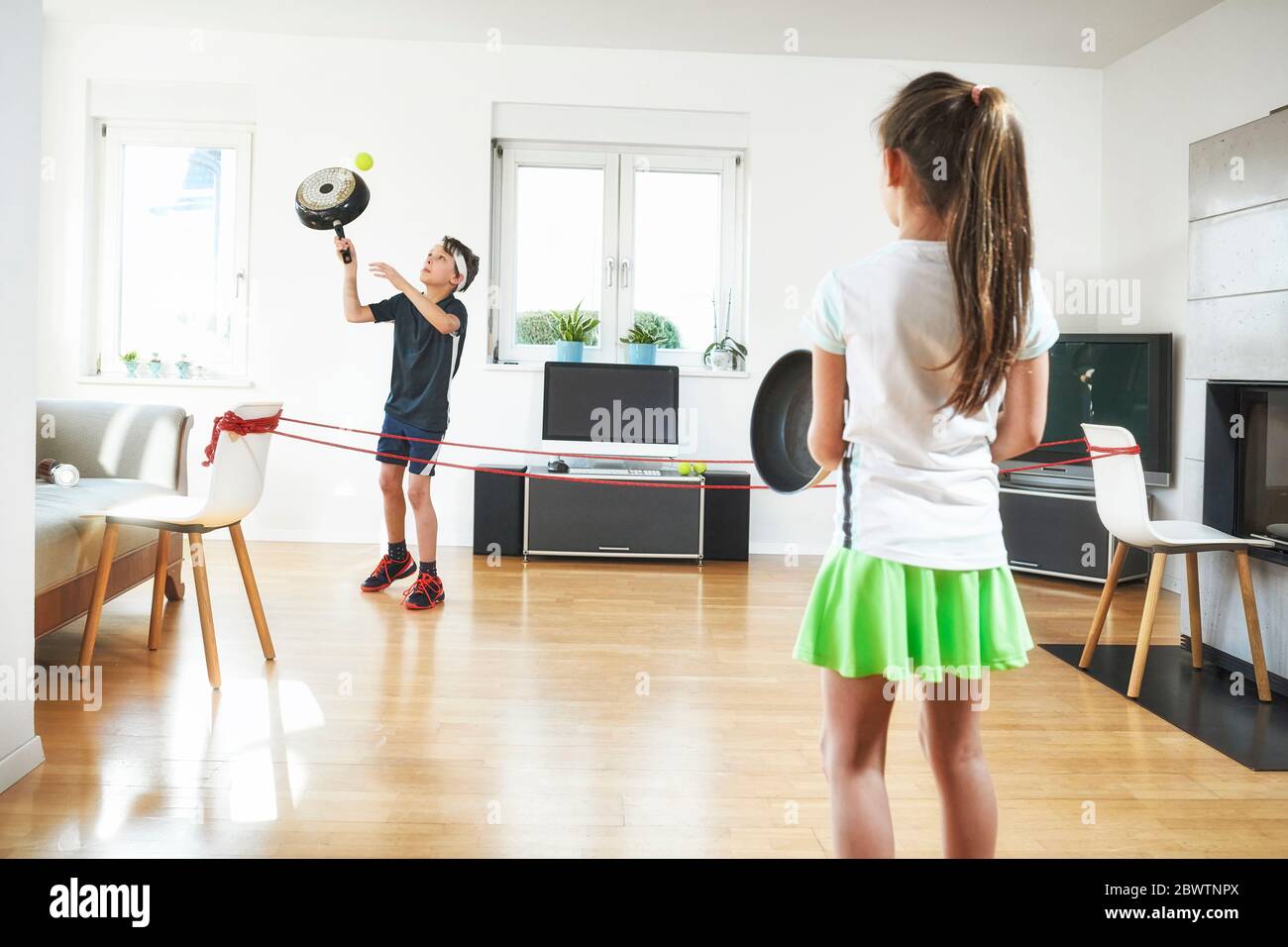 Bruder und Schwester spielen Tennis im Wohnzimmer zu Hause während Quarantäne Stockfoto