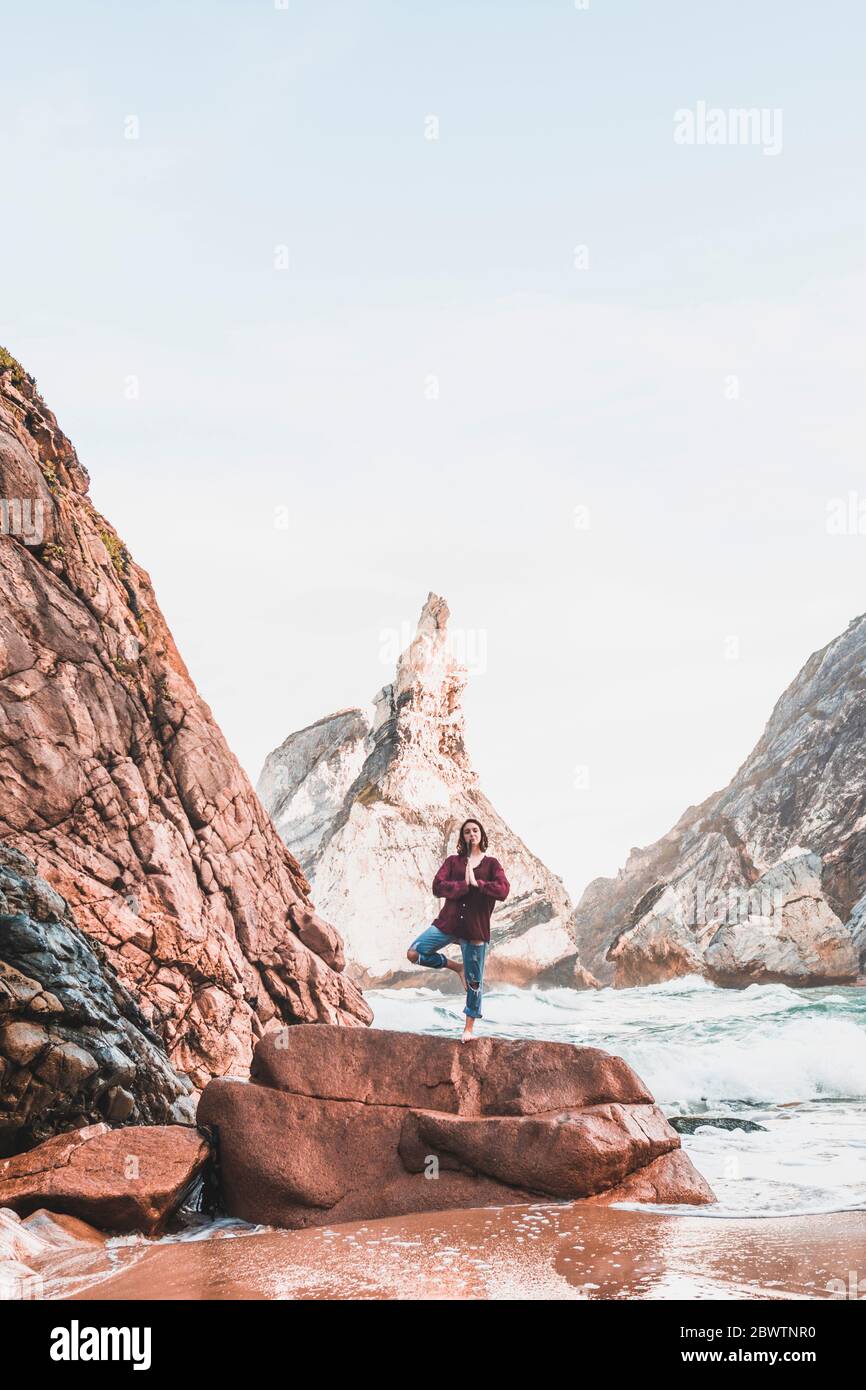 Junge Frau auf Felsen, Baumstellung, Praia da Ursa, Lissabon, Portugal Stockfoto