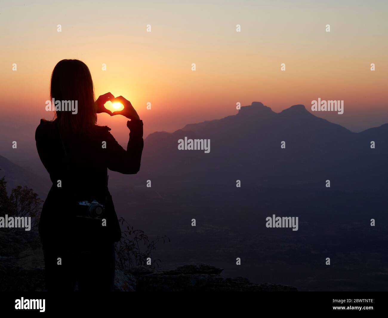Silhouette einer Frau, die bei Sonnenuntergang mit ihren Händen das Herz formt, Serra da Leba, Angola Stockfoto