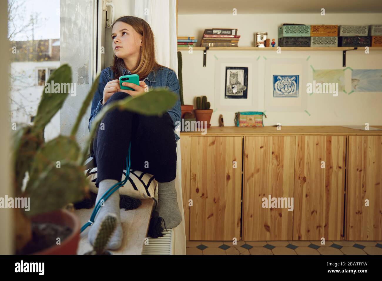 Mädchen sitzt am Fenster zu Hause halten Smartphone Stockfoto