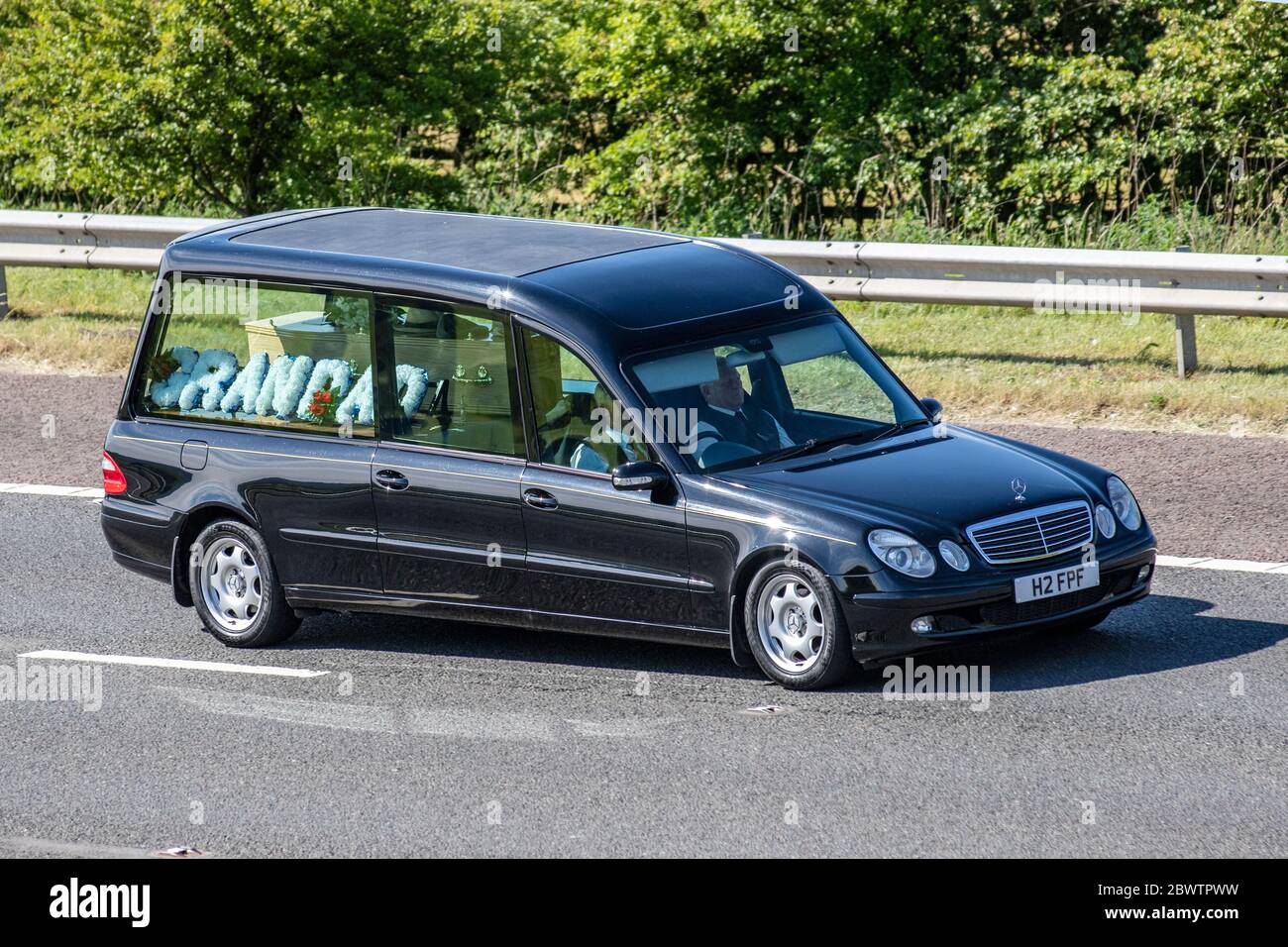 Bestattungswagen mit Großvater Bouquet; Fahrzeug Verkehr bewegenden Fahrzeugen, Bestatter fahren Fahrzeug auf UK Straßen, Opa Bestattungsmotoren auf der Autobahn M6 Autobahn Stockfoto