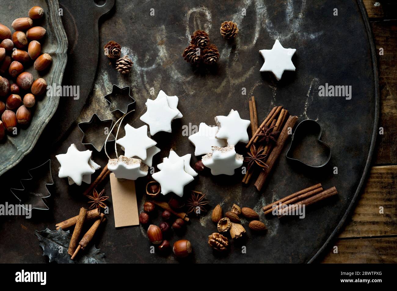 Rustikales Backblech, Zimtstangen, sternförmige Weihnachtskekse, Ausstechformen und Nüsse Stockfoto