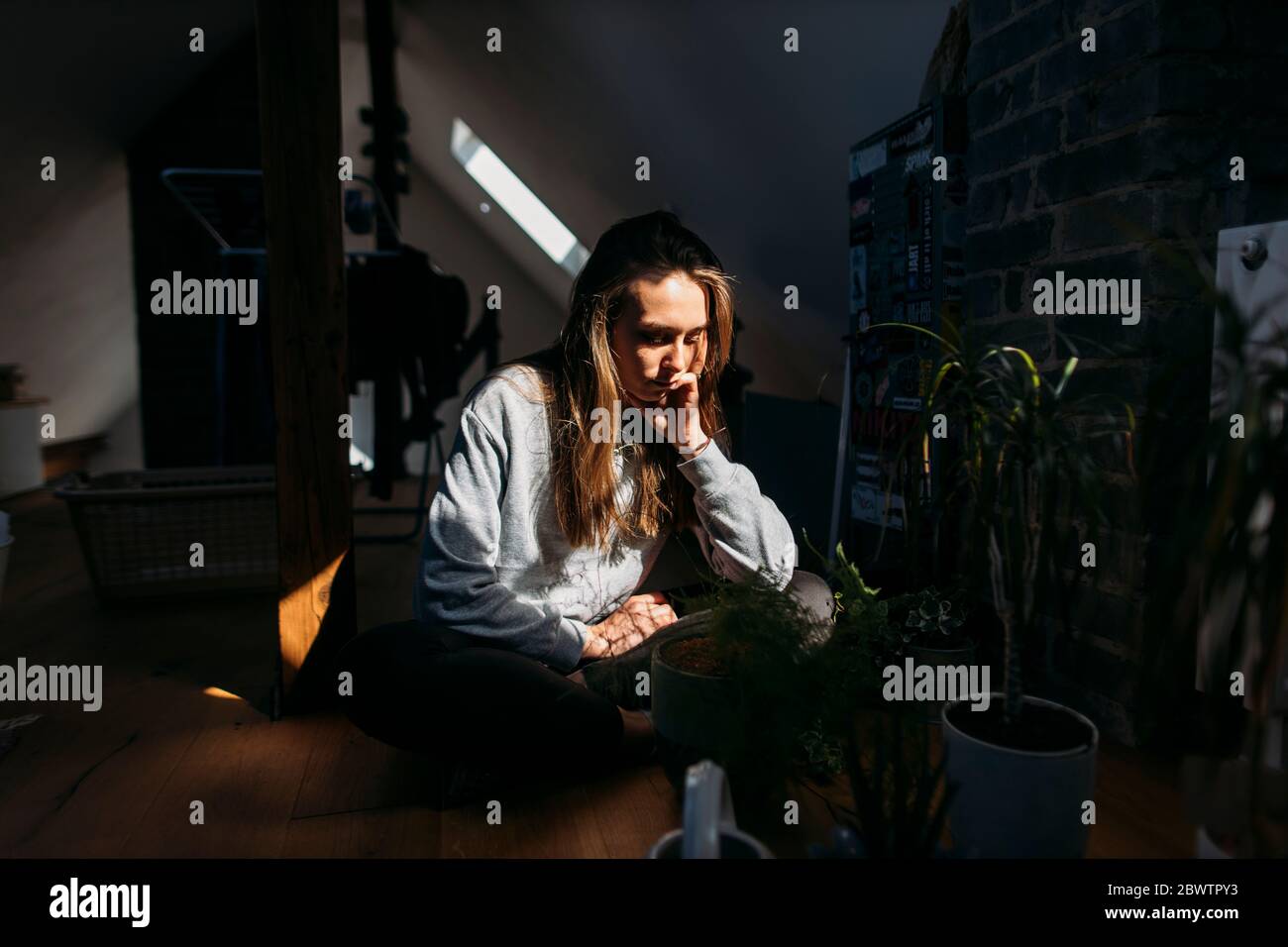 Seriöse junge Frau auf dem Dachboden mit Pflanzen sitzen Stockfoto