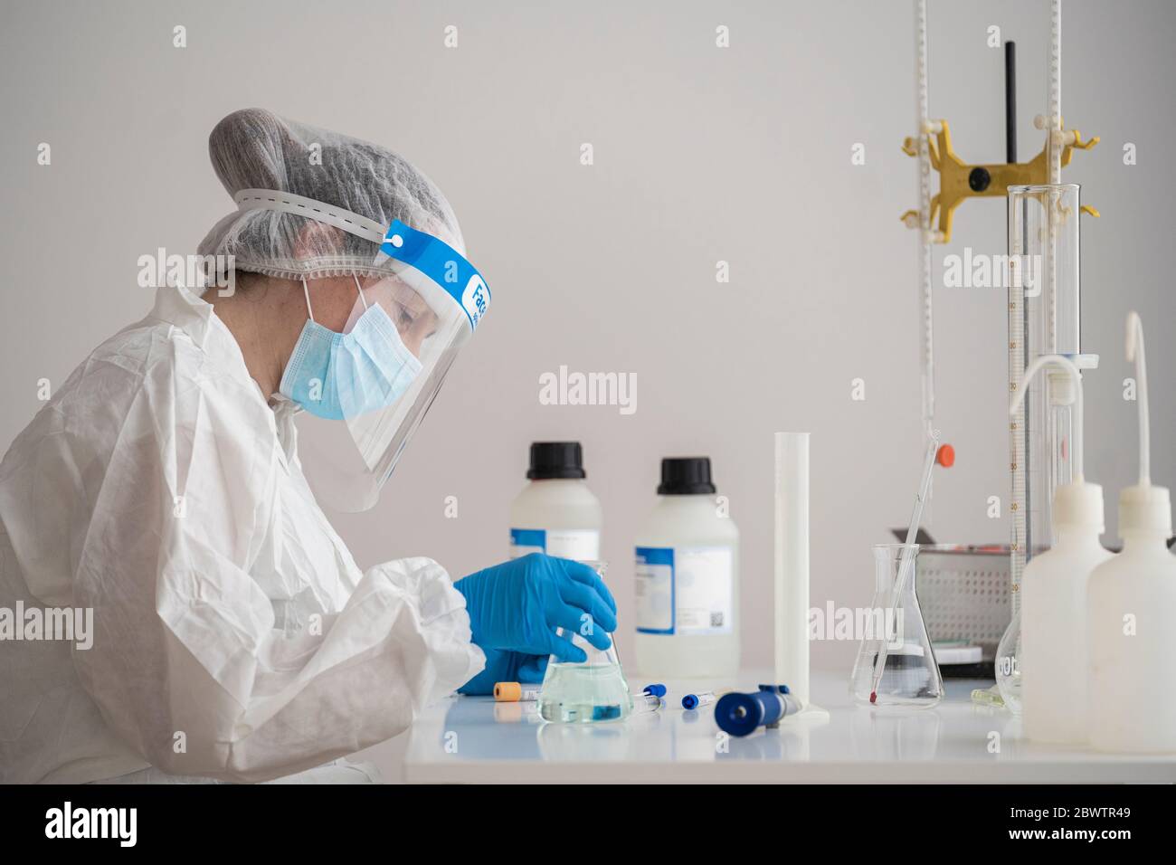 Frau in Schutzkleidung sitzt am Schreibtisch Forschung über Epidemiologie Stockfoto