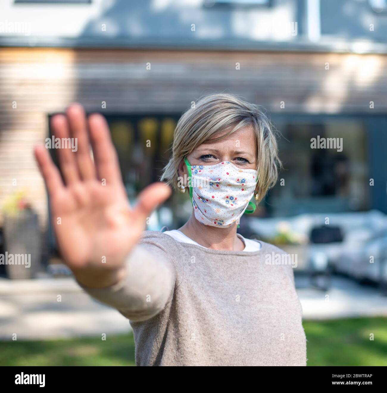 Portrait der Frau trägt Schutzmaske Gesicht beim Stehen mit Stop-Geste gegen Haus während der Isolation Stockfoto