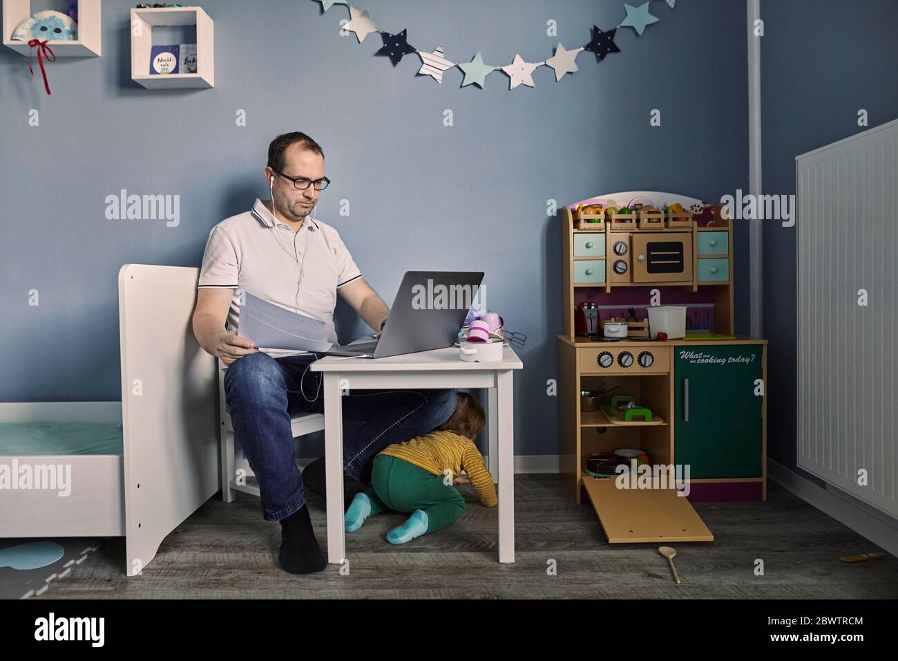 Mann arbeitet und mit Laptop im Kinderzimmer mit gleichzeitiger Kinderbetreuung Stockfoto