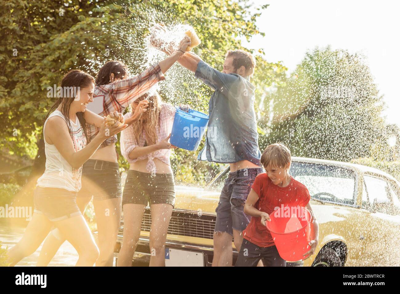 Gruppe von Freunden waschen gelben Oldtimer im Sommer Spaß Stockfoto