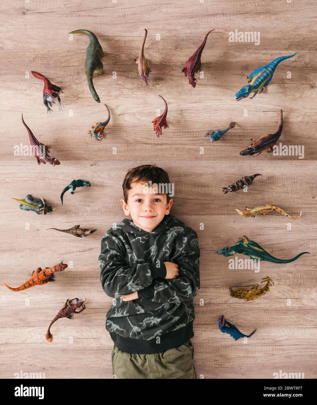 Porträt eines lächelnden kleinen Jungen, der zwischen Spielzeug-Dinosauriern auf dem Boden liegt Stockfoto