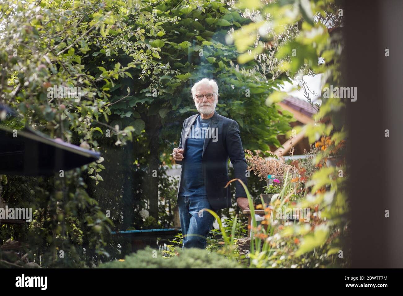 Älterer Mann, der im Garten Zigarette raucht Stockfoto