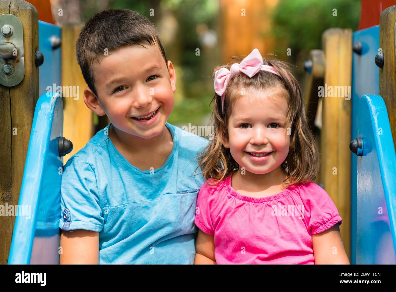 Porträt des glücklichen kleinen Jungen und seiner jüngeren Schwester sitzen zusammen auf Spielplatz Rutsche Stockfoto