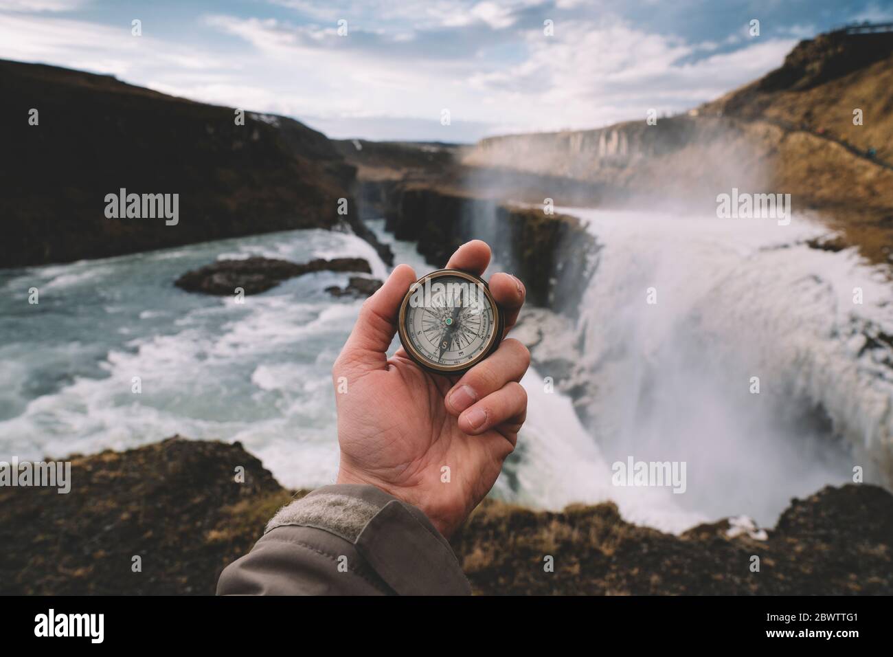 Island, Hand der Person hält Navigationskompass gegen spritzt Gullfoss Wasserfall Stockfoto