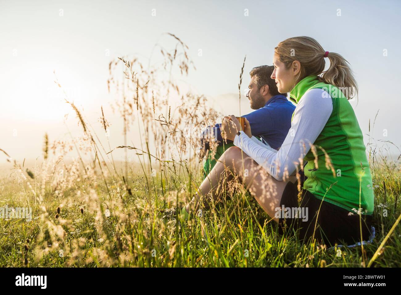 Ehepaar sitzt auf einer Wiese in den Bergen bei Sonnenaufgang, Achenkirch, Österreich Stockfoto
