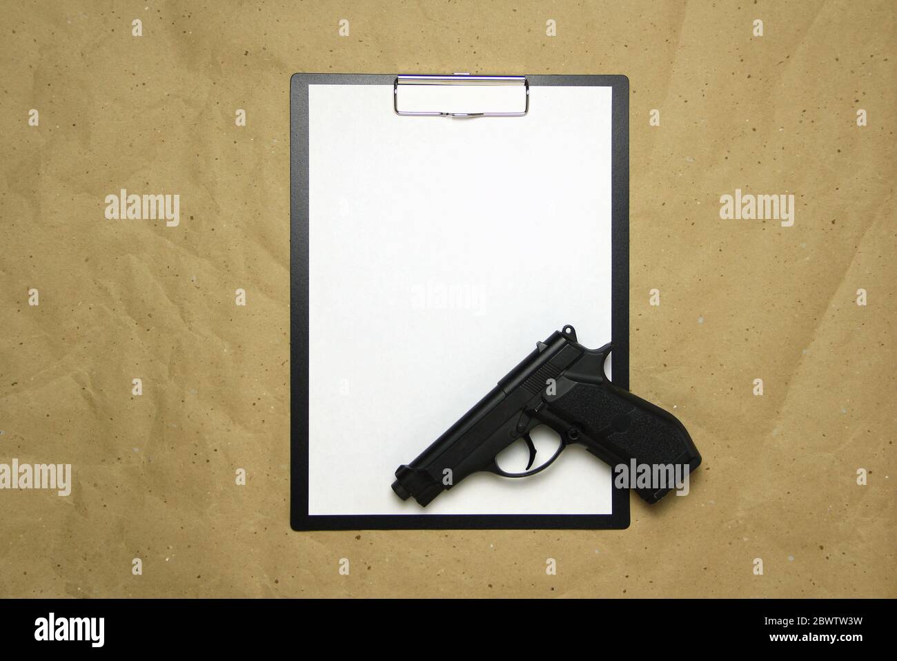 Ein Tablett mit einem weißen Blatt im A4-Format mit Pistole auf einem beigen Bastelpapier. Konzept des Rechtssystems, kriminelle Organisationen, Sicherheitsdienste. Stock Foto mit leerem Platz für Ihren Text und Design. Stockfoto