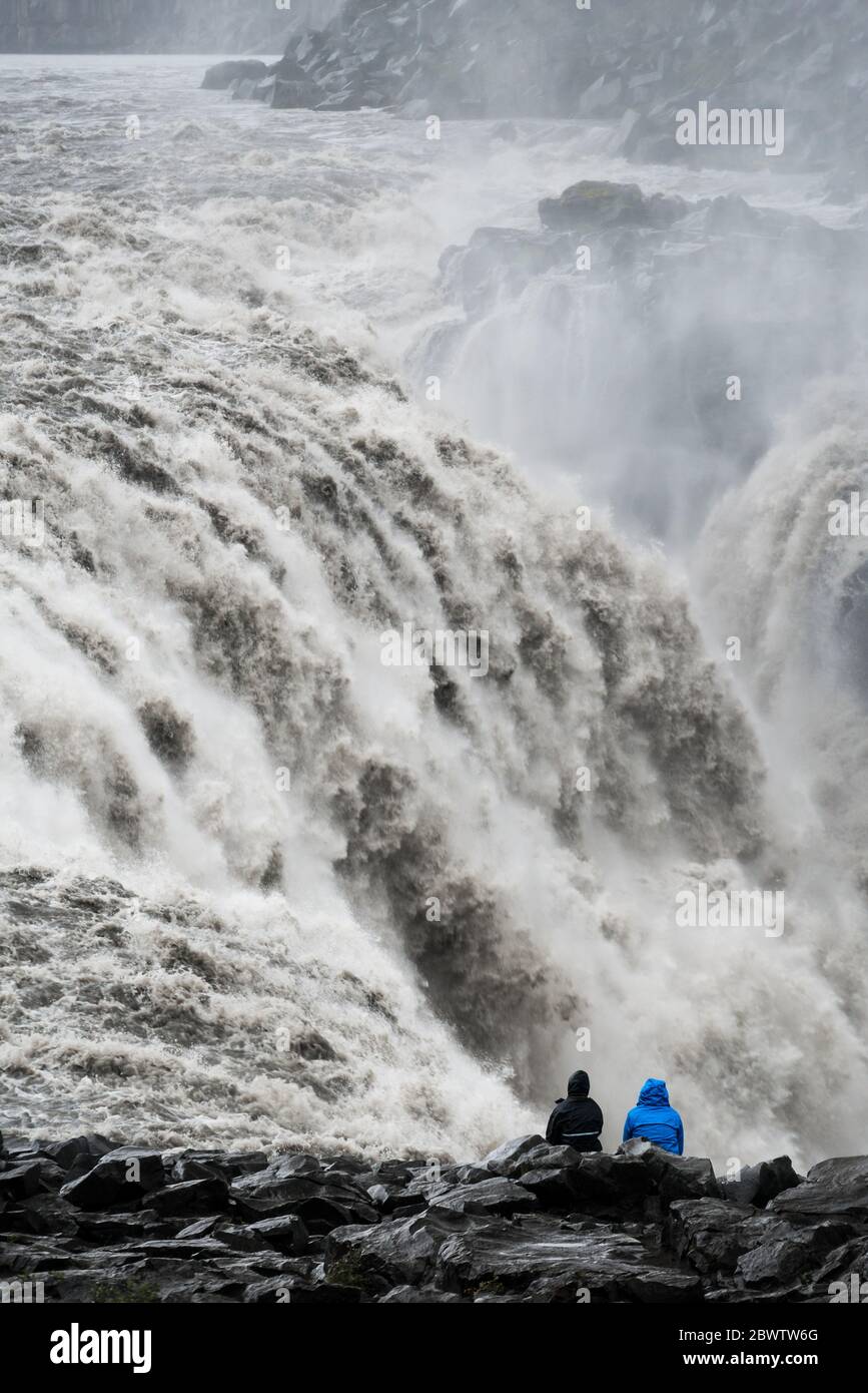 Nahaufnahme eines wütenden isländischen Wasserfalls mit einem schwarzen Felsstrand im Vordergrund Stockfoto