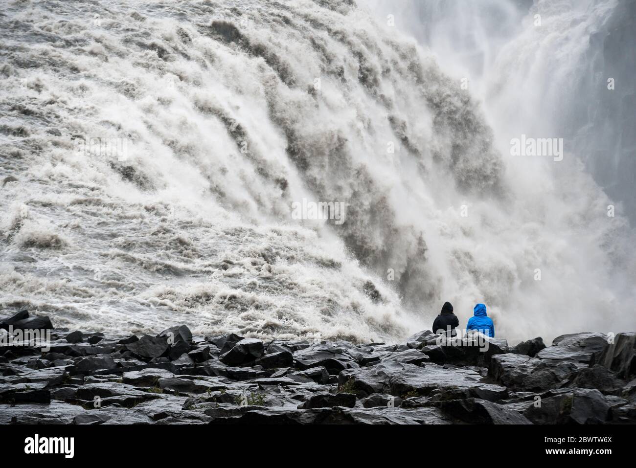 Nahaufnahme eines wütenden isländischen Wasserfalls mit einem schwarzen Felsstrand im Vordergrund Stockfoto