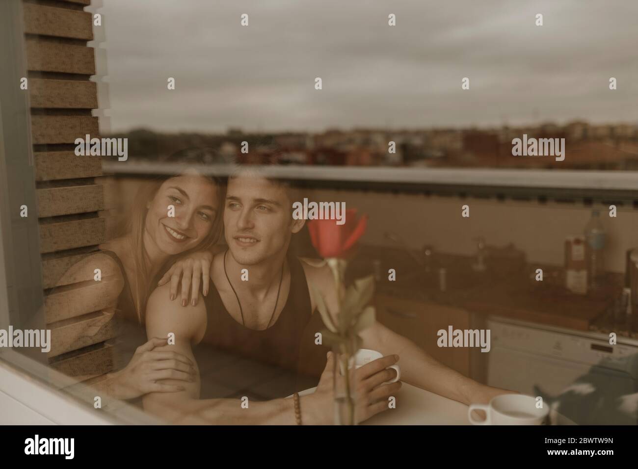 Romantisches junges Paar mit roter Rose hinter Fensterscheibe Stockfoto