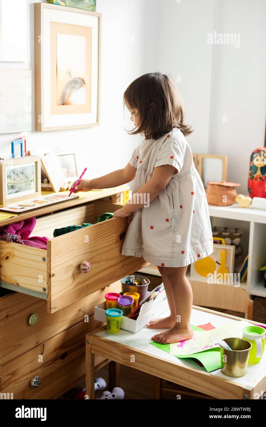 Volle Länge des Mädchens Zeichnung am Schrank, während auf dem Tisch im Haus stehen Stockfoto
