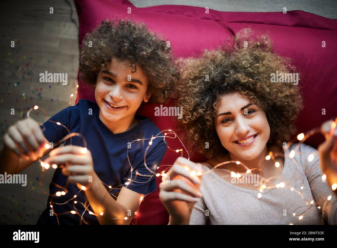 Mutter und Sohn liegen auf dem Boden und spielen mit Lichterketten Stockfoto