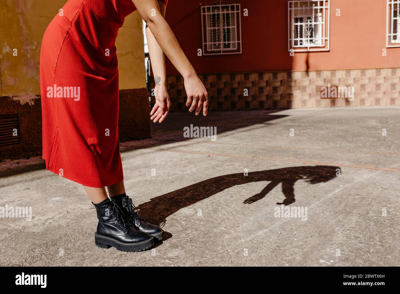 Junge Frau in rotem Kleid und schwarzen Stiefeln, die mit ihrem Schatten auf dem Boden spielt Stockfoto