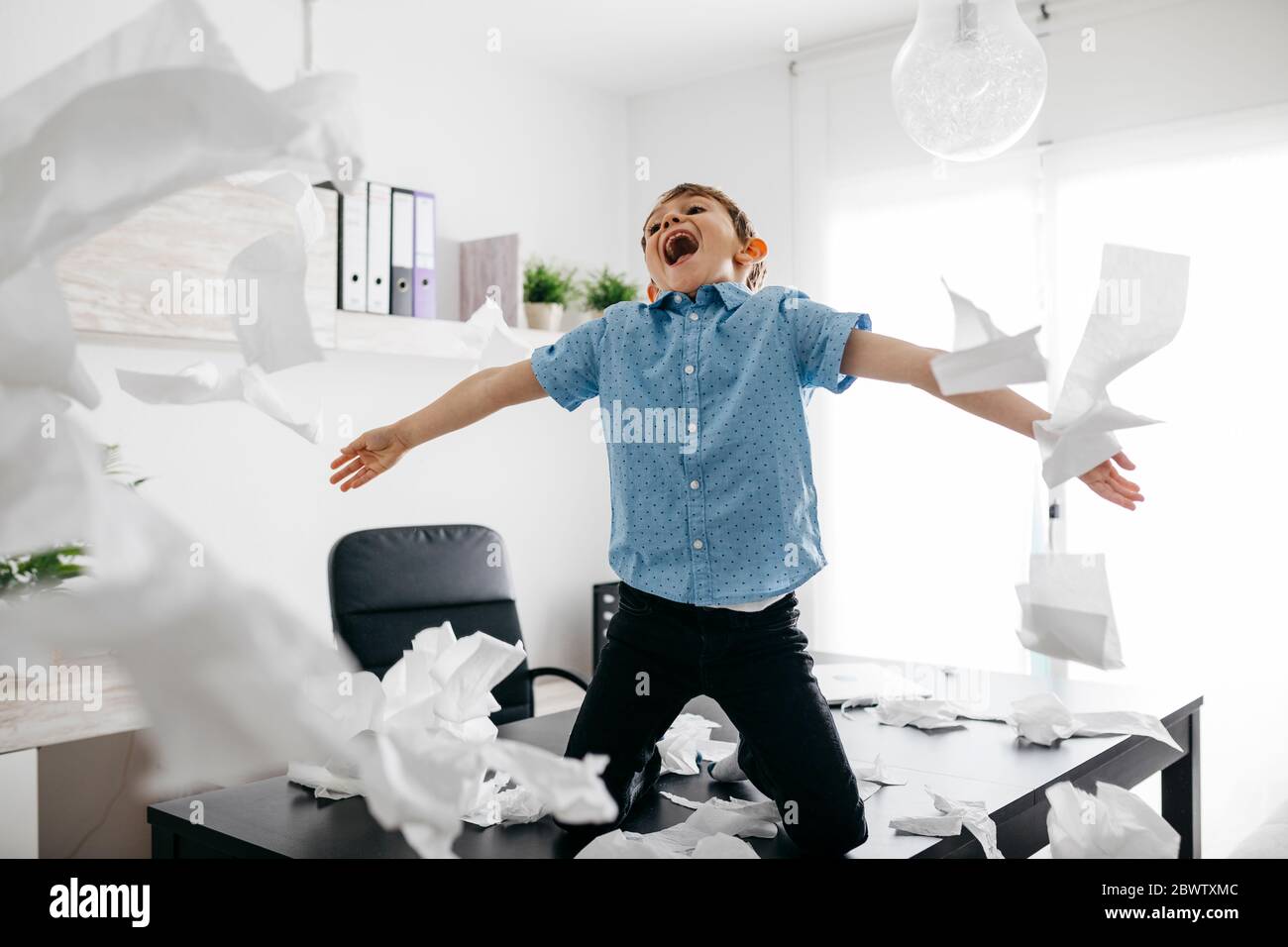 Schelmische Junge spielt mit Toilettenpapier auf dem Schreibtisch im Home Office Stockfoto