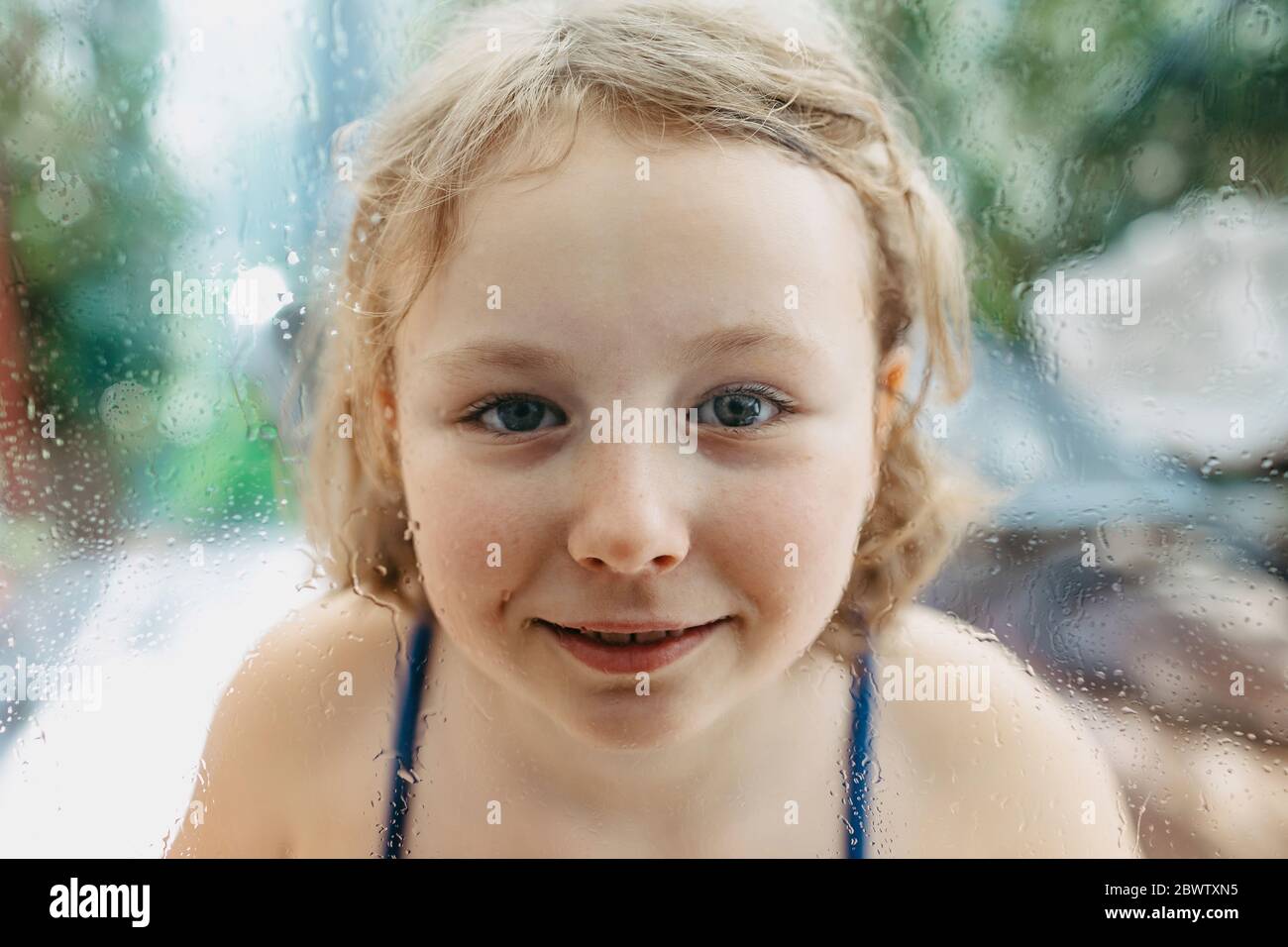 Portrait von lächelnd blonde Mädchen durch nasse Fensterscheibe suchen Stockfoto