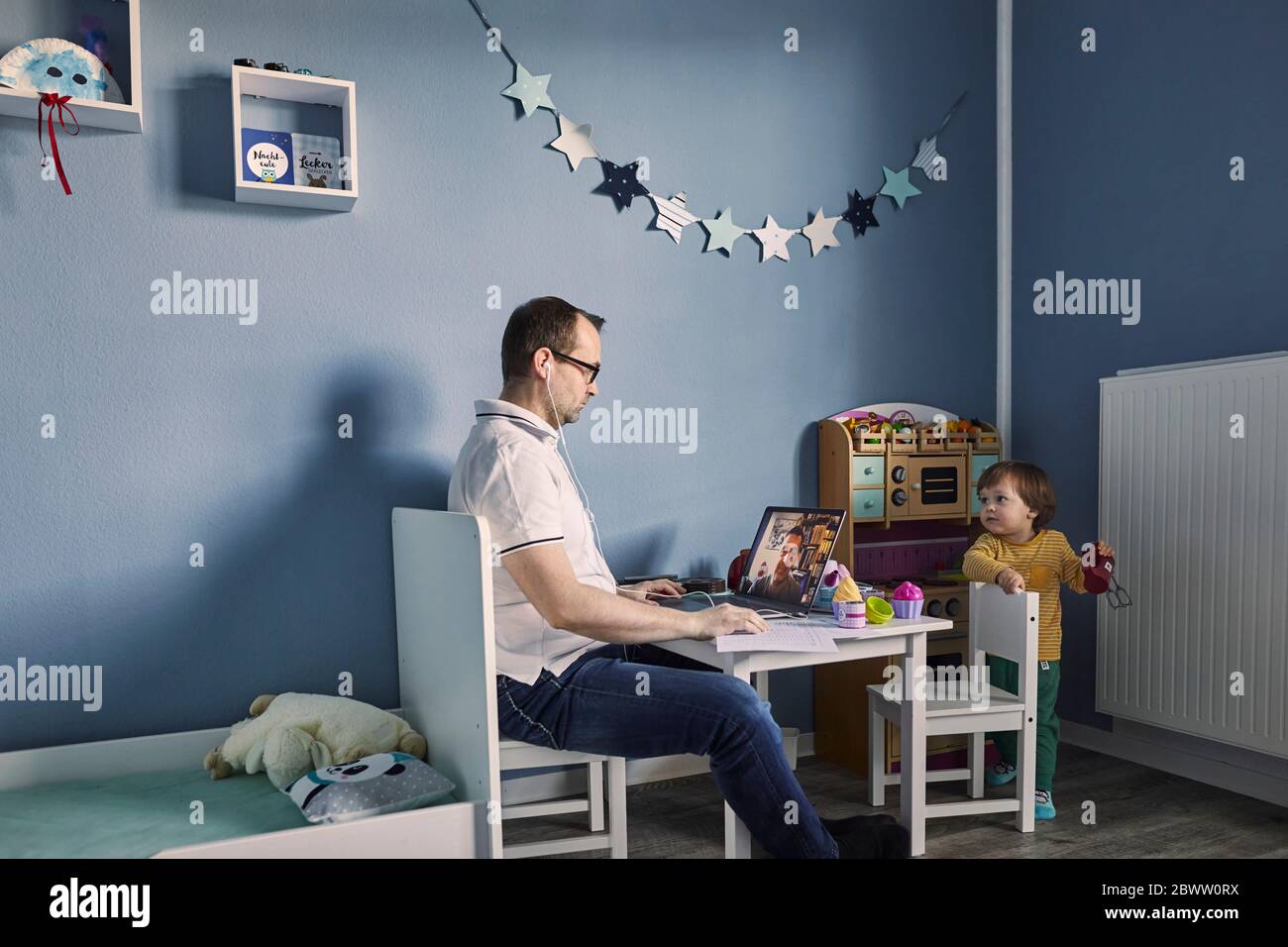 Mann arbeitet und mit Laptop im Kinderzimmer mit gleichzeitiger Kinderbetreuung Stockfoto