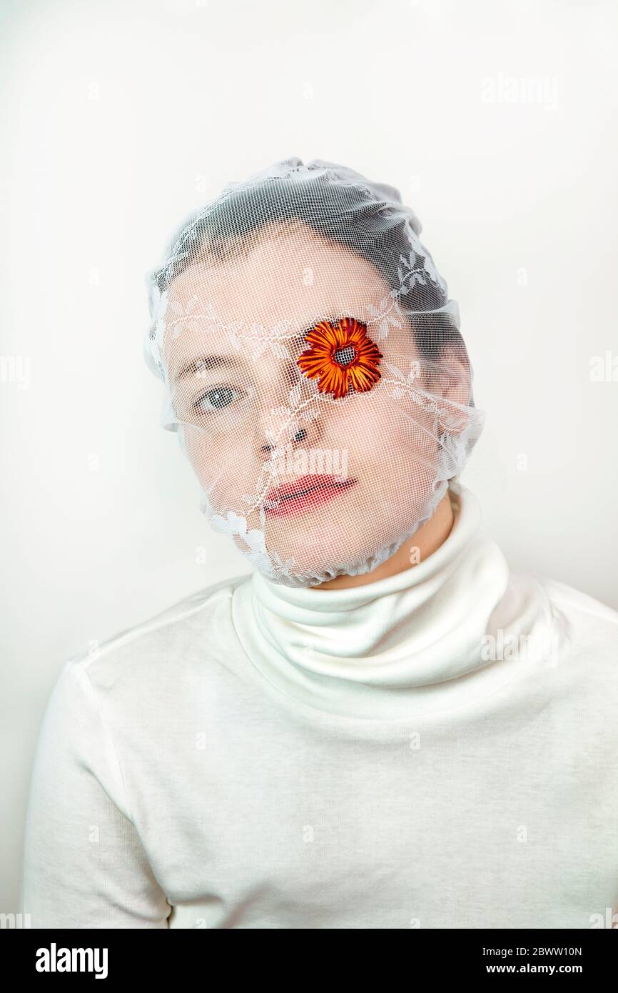 Portrait einer jungen Frau mit weißem Schleier und Blume, die ein Auge bedeckt Stockfoto