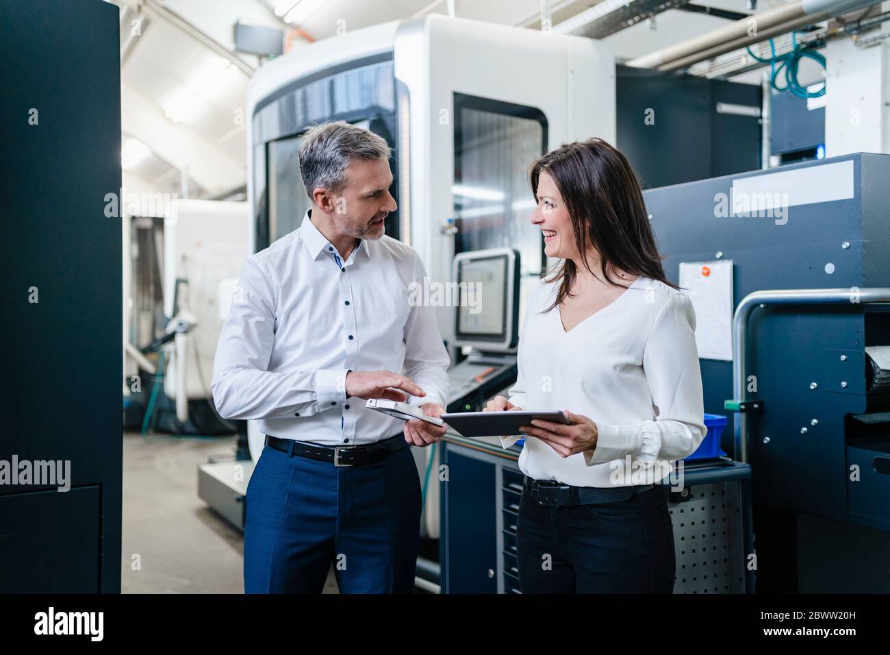 Geschäftsmann und Geschäftsfrau mit Produkt und Tablet mit einem Arbeitstreffen in einer Fabrik Stockfoto