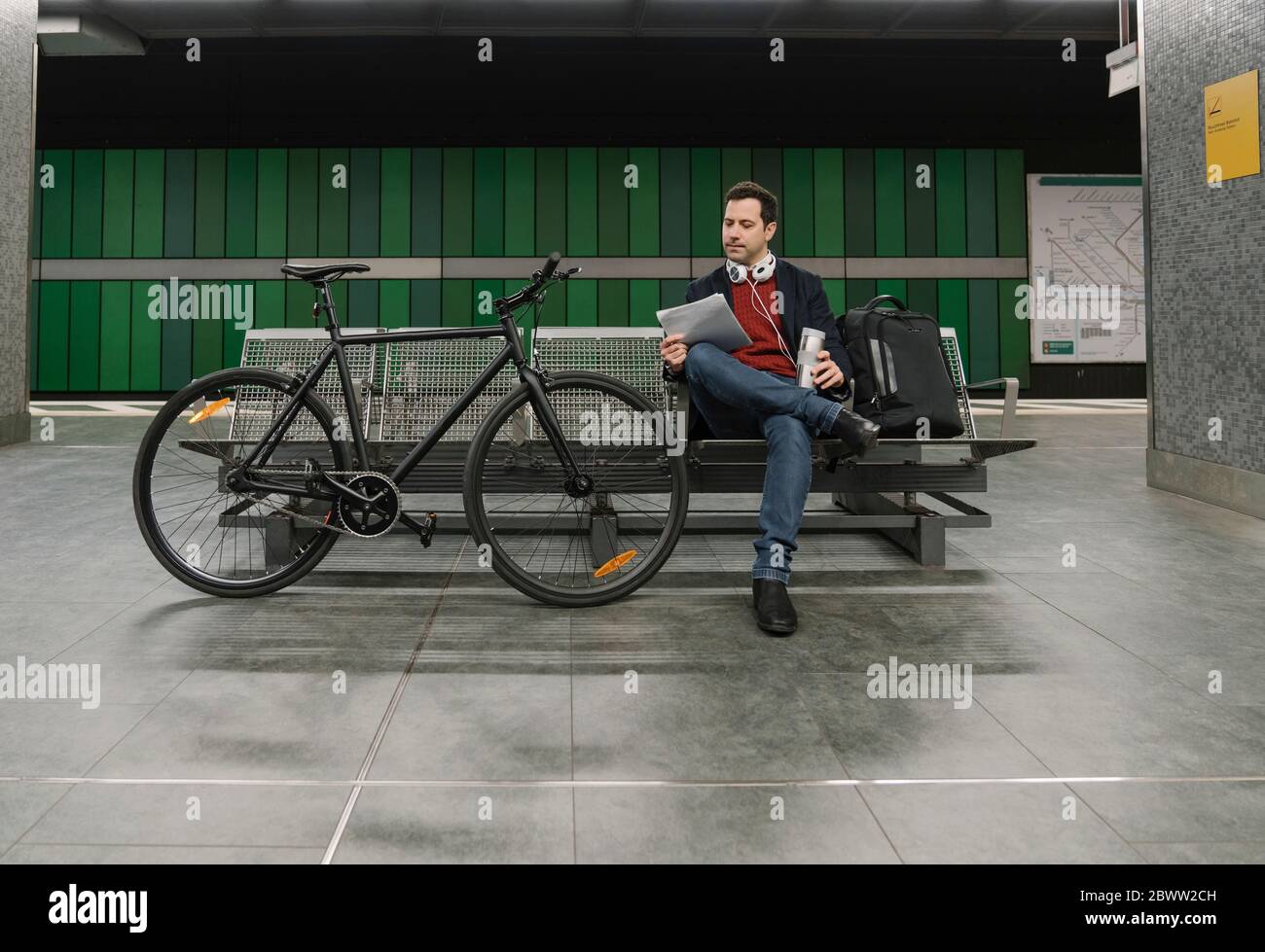 Volllänge der Geschäftsmann mit Dokument sitzt auf Bank mit dem Fahrrad an der U-Bahn-Station in Frankfurt, Deutschland Stockfoto