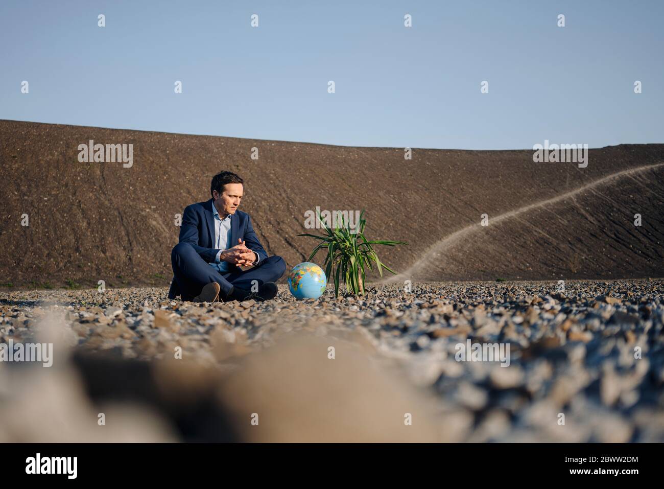 Reifer Geschäftsmann sitzt auf einer stillgeblachten Mine Spitze mit Globeand Pflanze Stockfoto