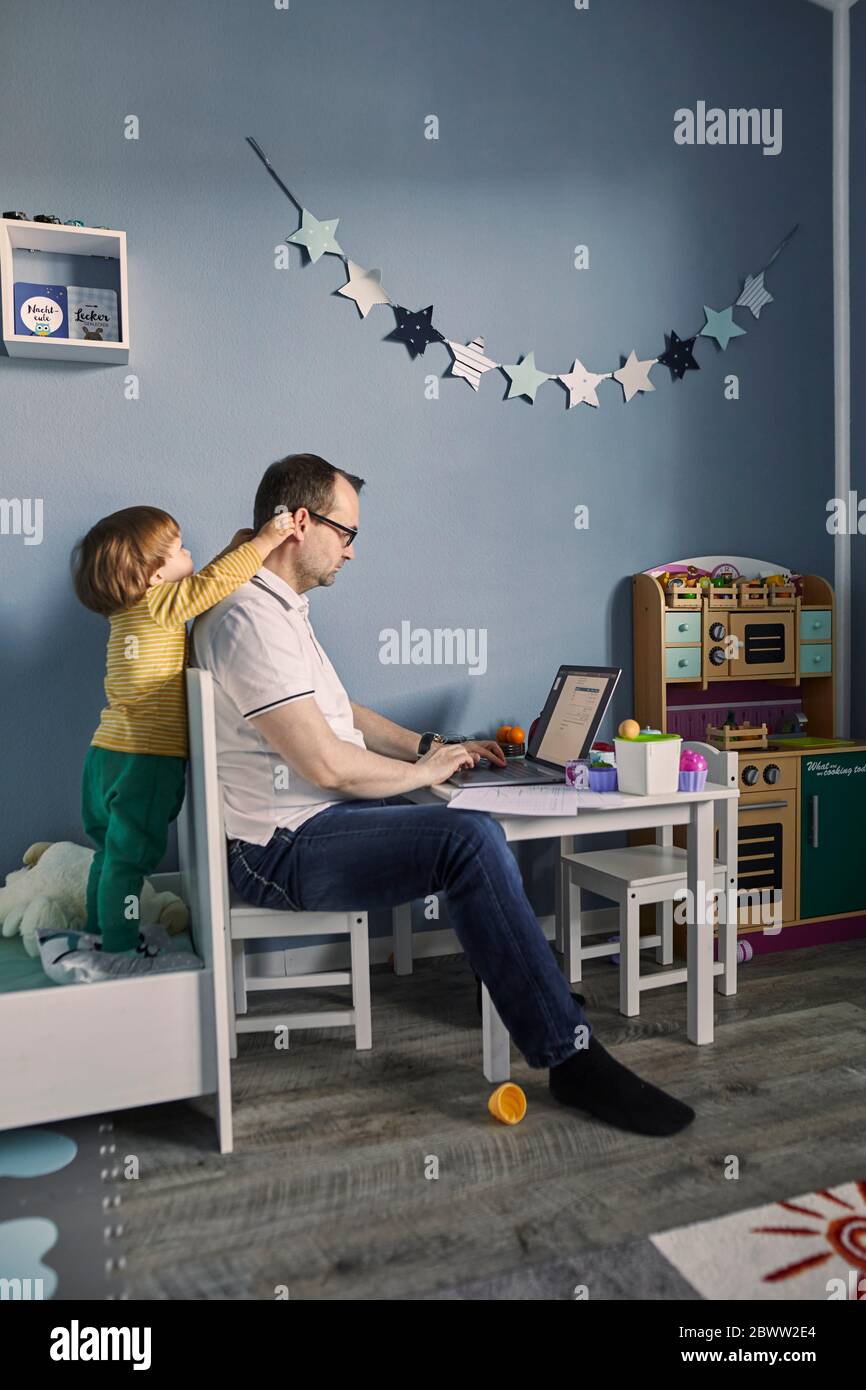 Mann arbeitet und mit Laptop im Kinderzimmer mit gleichzeitiger Kinderbetreuung Stockfoto