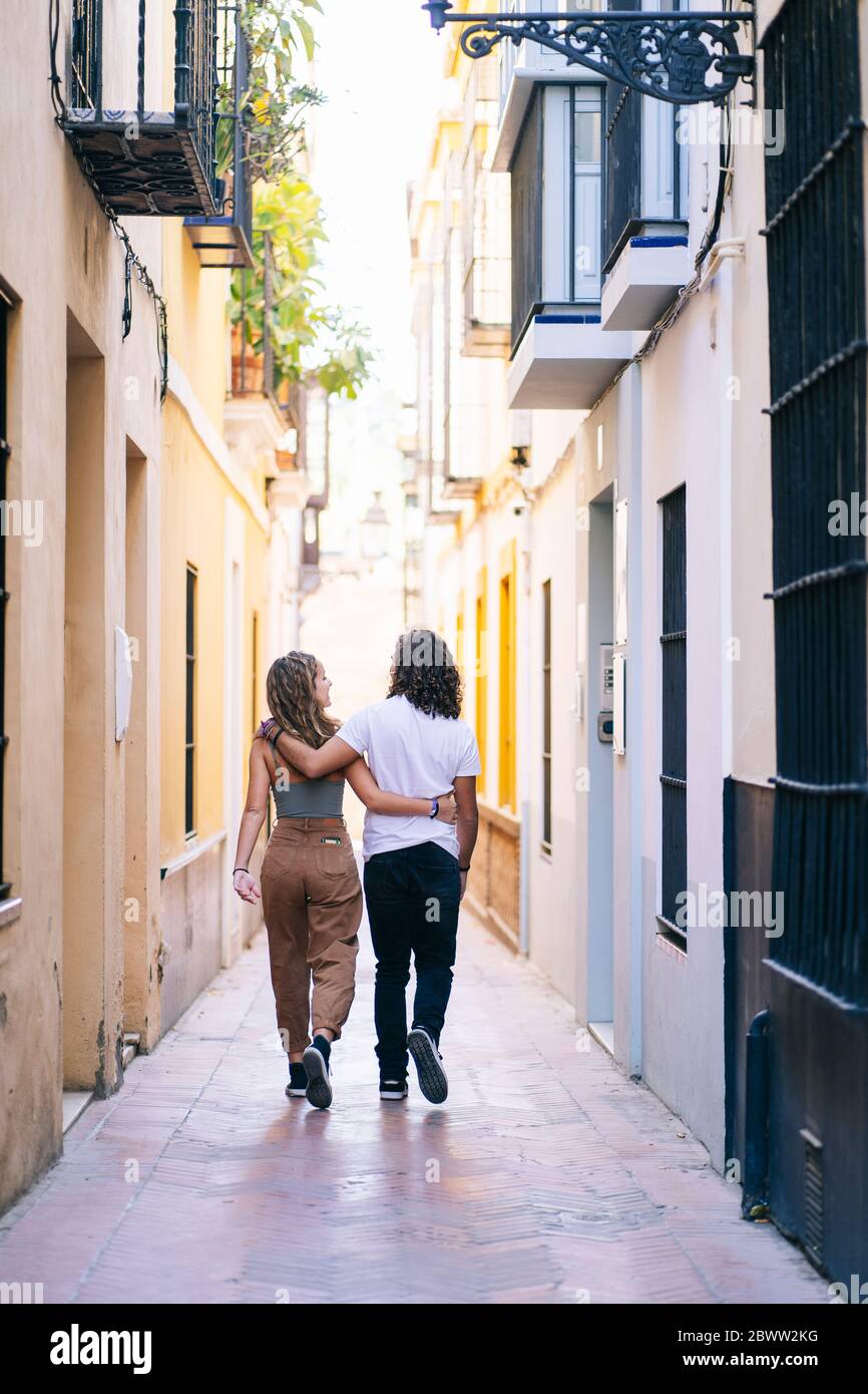 Rückansicht eines jungen Paares, das mit den Armen in der engen Straße in Santa Cruz, Sevilla, Spanien herumläuft Stockfoto