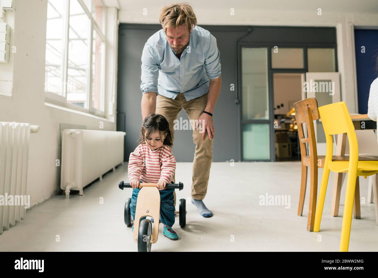 Vater beobachtete Tochter mit Laufrad Stockfoto