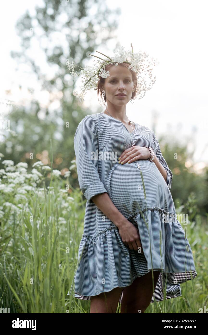 Portrait einer schwangeren Frau mit den Händen auf dem Bauch im Park stehend Stockfoto