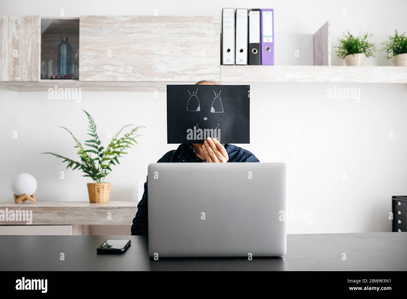 Mann, der zu Hause arbeitet, mit einem schwarzen Karton, der sein Gesicht bedeckt Stockfoto