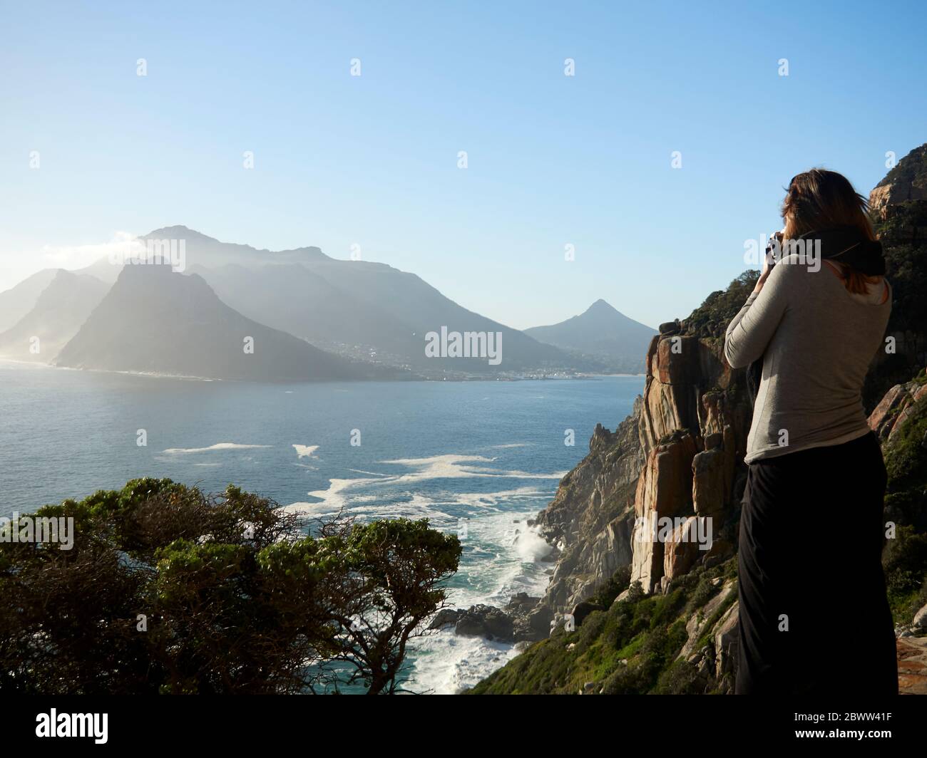 Frau, die Bilder von einer Berg- und Meereslandschaft macht, Chapman's Peak Drive, Südafrika Stockfoto
