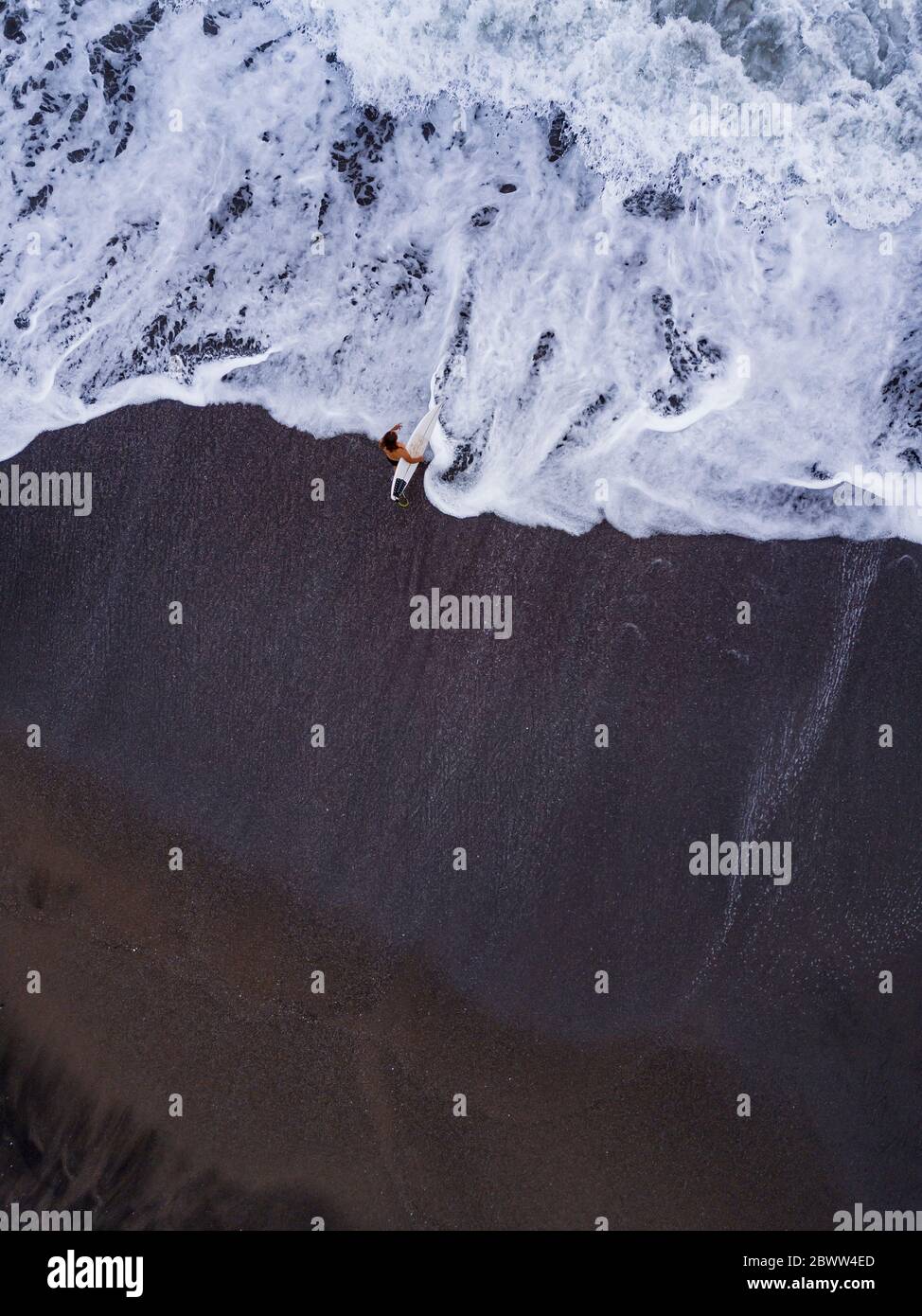 Indonesien, Bali, Pererenan Beach, Luftaufnahme des eineinmaligen Surfers am schwarzen Küstenstrand Stockfoto
