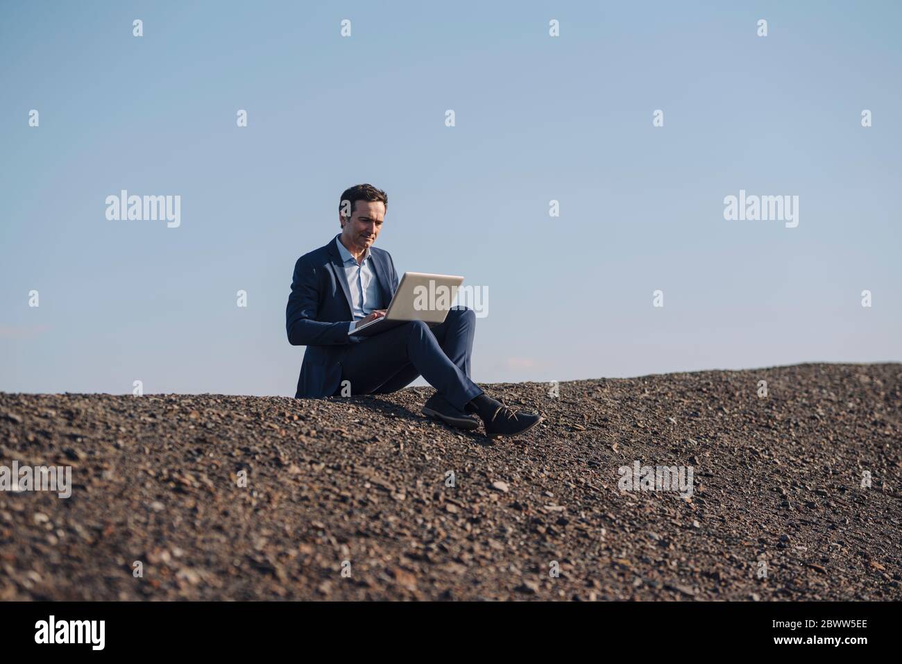 Reifer Geschäftsmann mit Laptop auf einem stillgetappten Mine Tipp Stockfoto