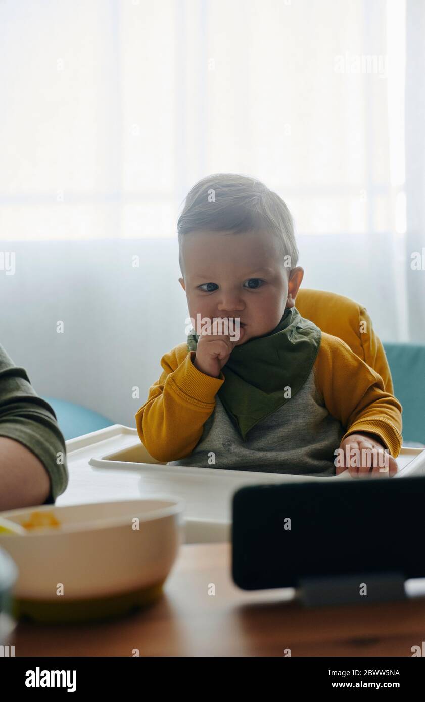 Portrait von Baby Junge sitzen im Hochstuhl Filme auf dem Smartphone Stockfoto