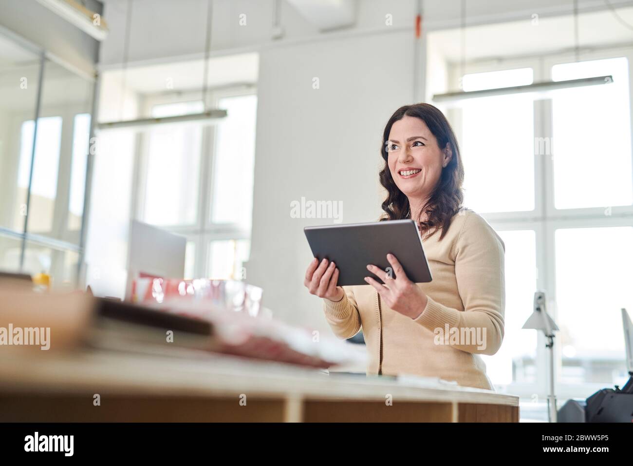 Lächelnder Unternehmer mit digitalen Tablet, während am Schreibtisch am Arbeitsplatz stehen Stockfoto