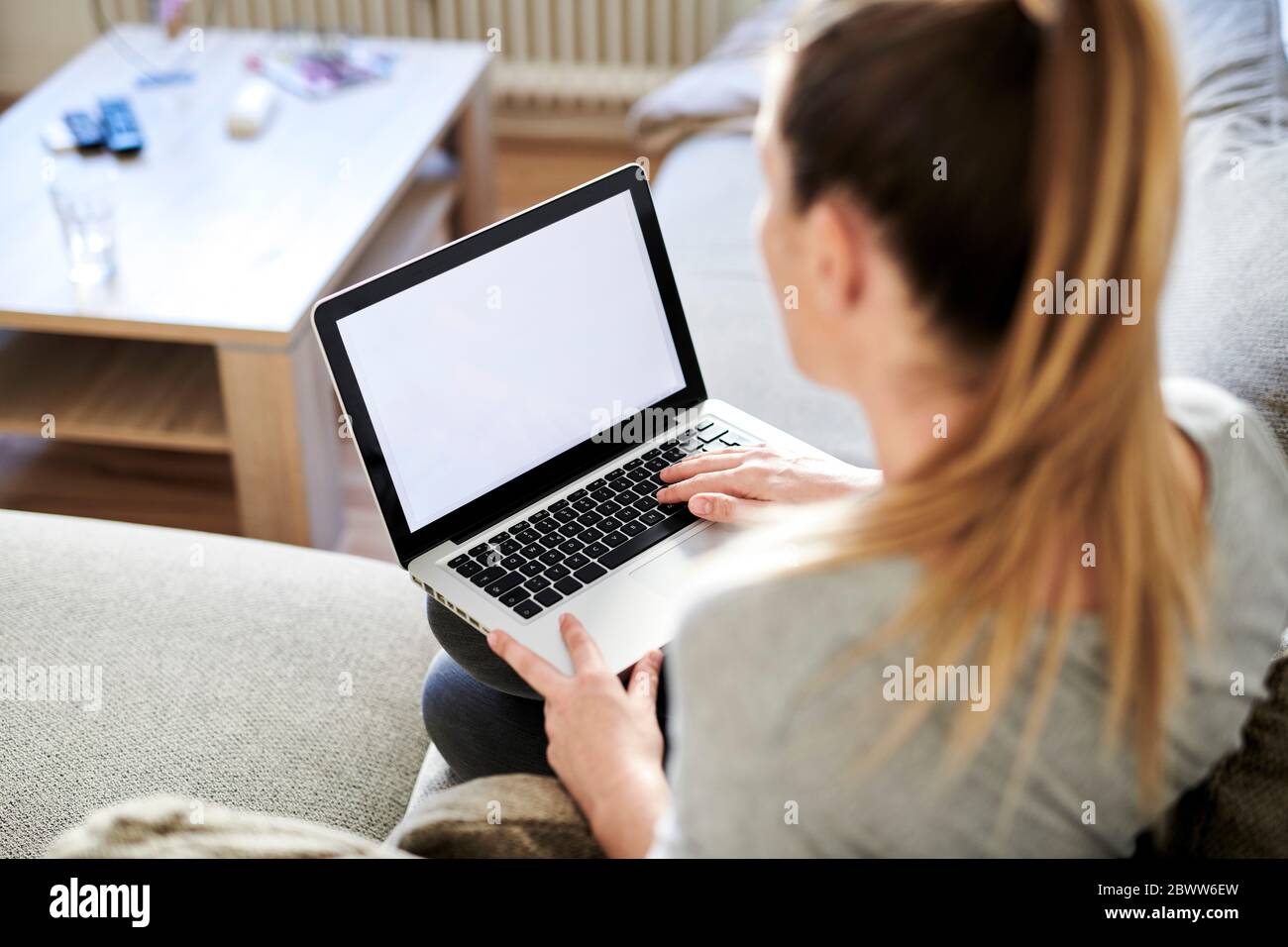 Blick auf Frau mit Laptop, während sie auf dem Sofa zu Hause sitzt Stockfoto