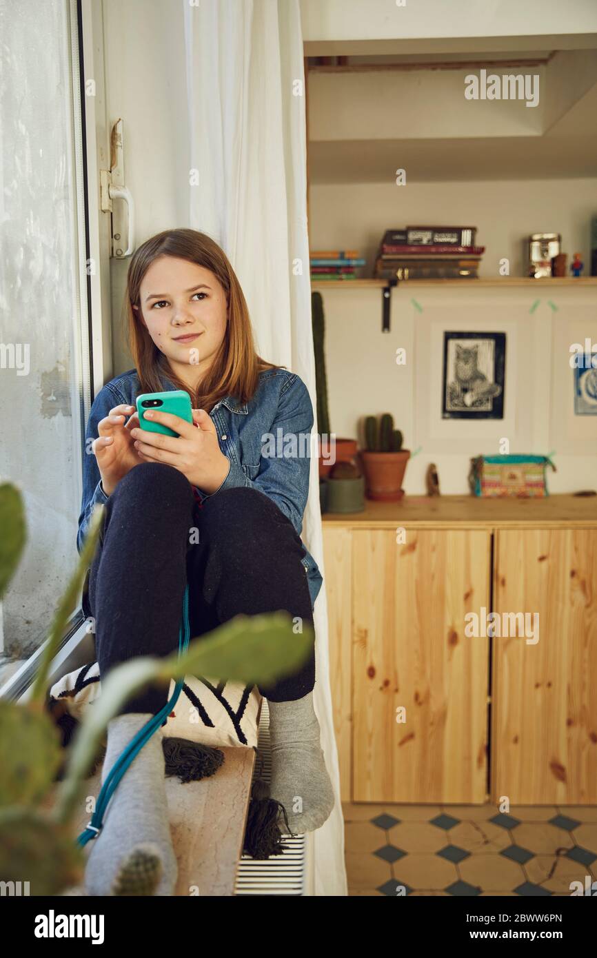 Mädchen sitzt am Fenster zu Hause halten Smartphone Stockfoto