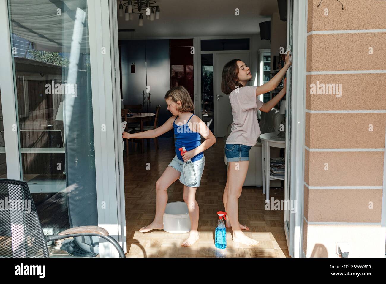 Zwei Schwestern putzen Glasscheiben von Terrassentüren Stockfoto