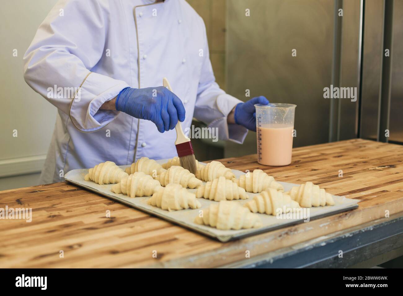 Letzte Vorbereitung vor dem Backen. Bäcker Lasurrosen Croissants mit Ei waschen Arbeit in seiner Küche mit Kochbürste Stockfoto
