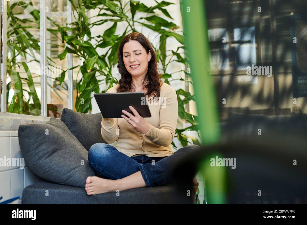 Lächelnder Unternehmer mit digitalen Tablet, während auf dem Sofa am Arbeitsplatz sitzen Stockfoto