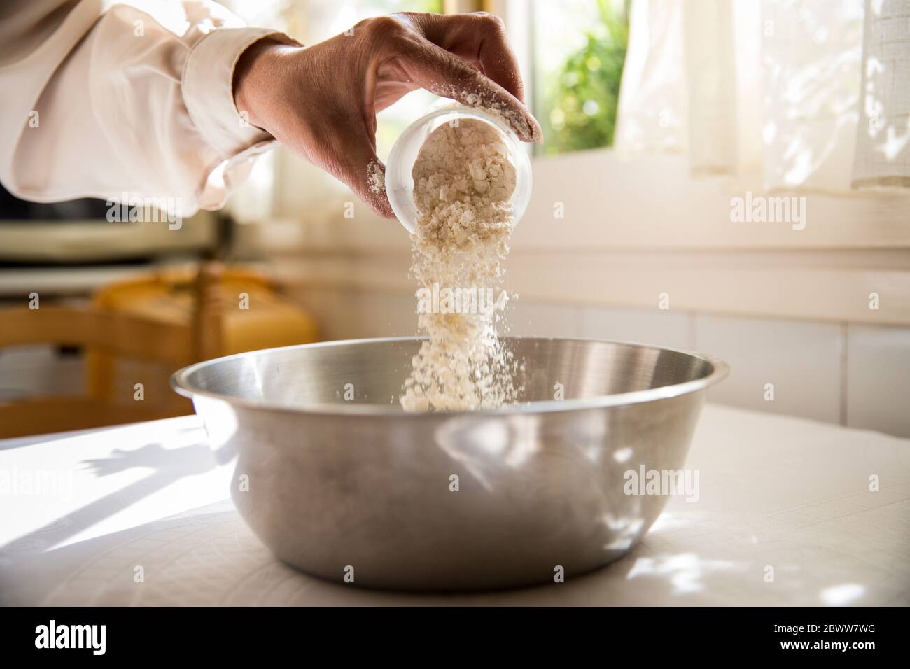 Hand der Frau, die Mehl in die Schüssel gießt Stockfoto