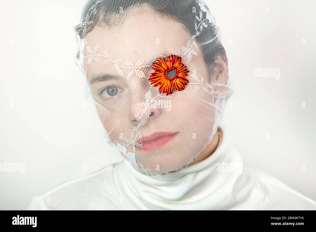 Portrait einer jungen Frau mit weißem Schleier und Blume, die ein Auge bedeckt Stockfoto